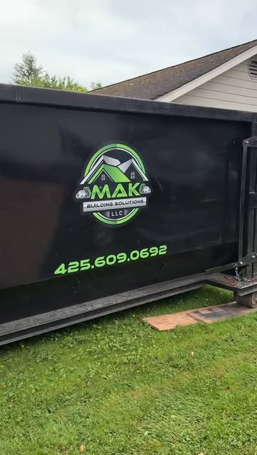MAK black dumpster positioned beside a home